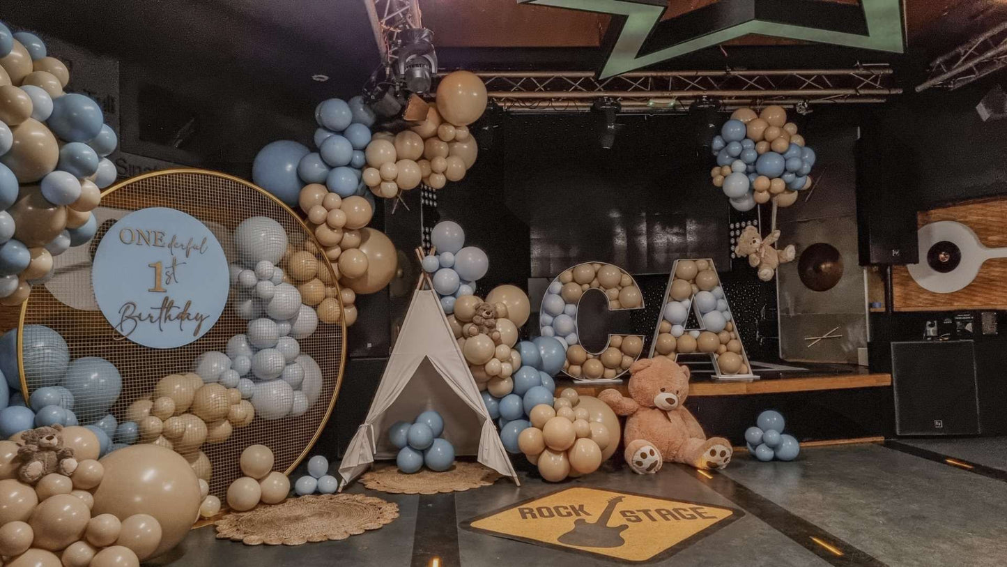 cort din panza alba si lemn pentru evenimente si petreceri copii, decorat cu baloane cu heliu si ursuleti de plus, un panou metalic auriu decorat cu baloane cu text personalizat si un cosulet cu ursulet de plus, legat cu baloane